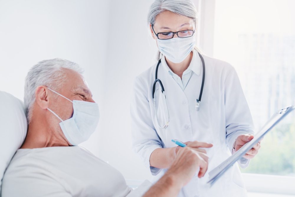 Old man sitting on hospital bed ang signing medical form to doctor in medical masks